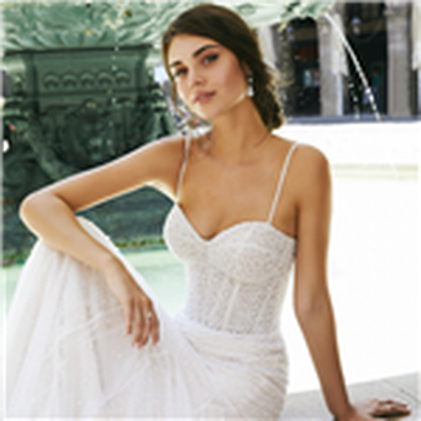 Thumbnail of a brunette model sat by an outside fountain in Ronald Joyce 69712, an exquisitely pearl and crystal-beaded fit and flare gown in glitter tulle with delicate straps and a sweetheart neckline